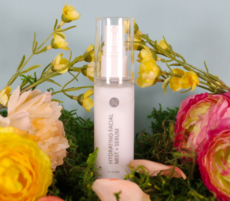 Neora’s Hydrating Facial Mist sitting in a bed of spring flowers.
